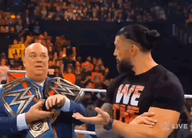 two men are standing next to each other in a wrestling ring . one of the men is wearing a we shirt .