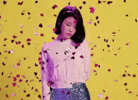 a woman in a white sweater and a sequined skirt is surrounded by confetti .