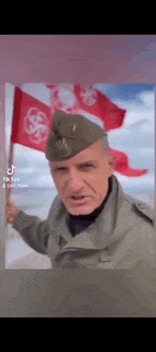 a man in a military uniform is holding a red flag in front of a wall .