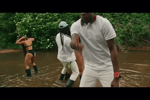 a man in a white shirt is standing in a river with two women in bikinis .