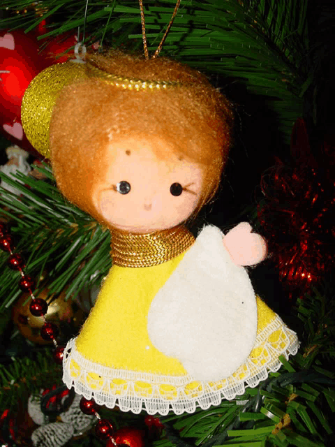 a stuffed angel hanging on a christmas tree with a red ball in the background