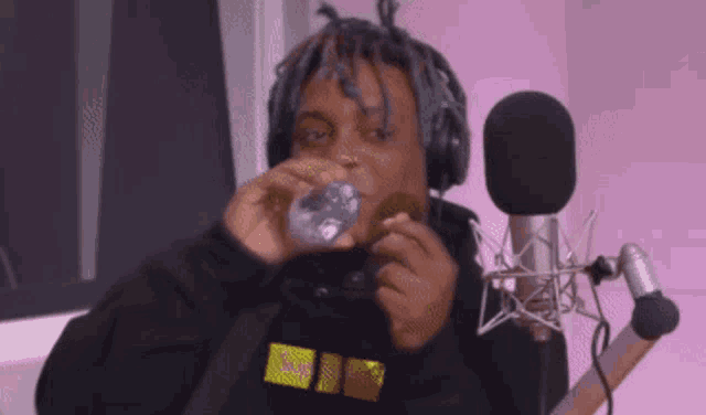 a man wearing headphones is sitting in front of a microphone drinking water .