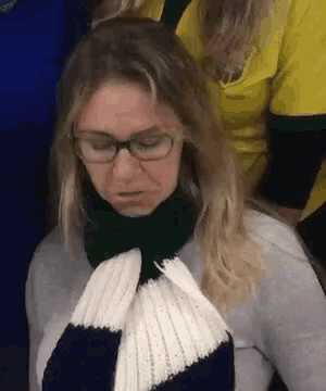 a woman wearing glasses and a scarf is looking down .