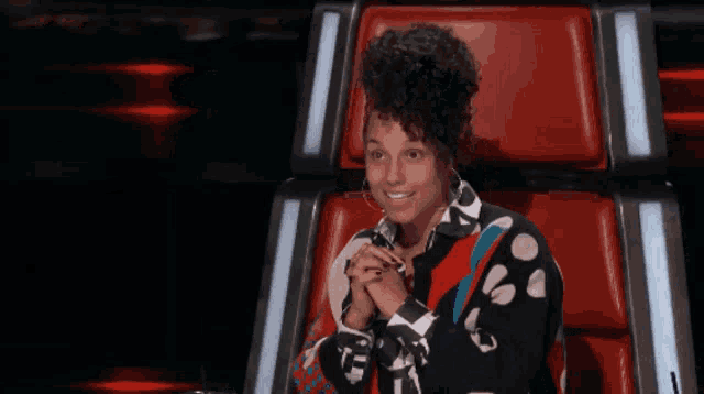 a man and a woman sit in a row of red chairs while a woman stands behind them