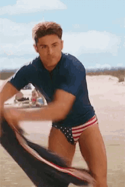 a man in a blue shirt and red white and blue swim trunks is holding a surfboard .