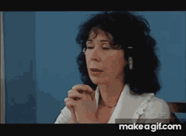 a woman with black hair and glasses is praying with her hands folded in front of her face .