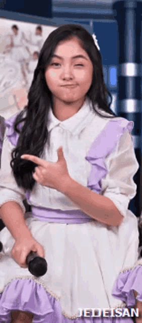 a girl in a white and purple dress is holding a microphone