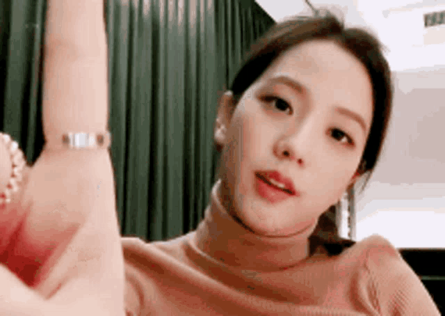 a woman wearing a turtleneck sweater and a bracelet is giving a thumbs up sign .