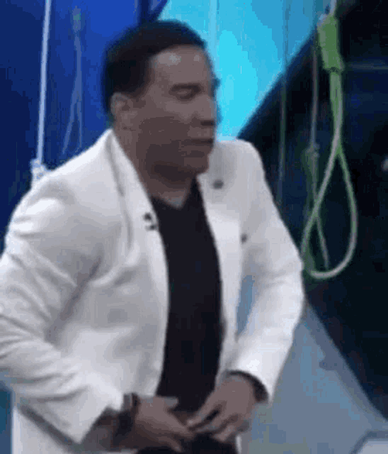 a man in a white suit and black shirt is standing in front of a rope hanging from a ceiling .