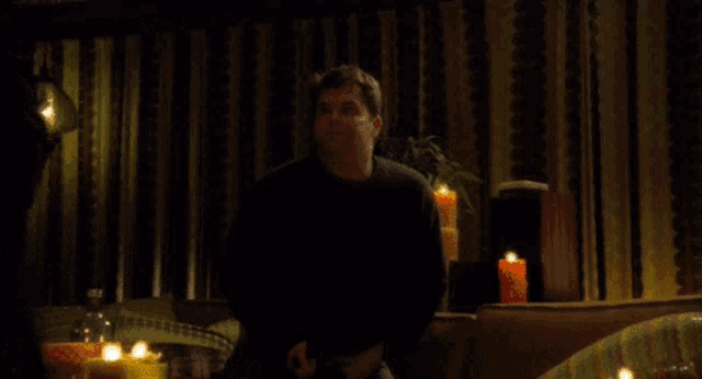 a man is sitting in a dark room with candles and the word anything behind him
