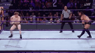 two wrestlers are in a ring with a referee in front of a crowd with the number 2 on it