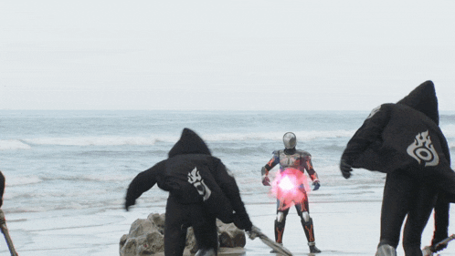a group of people standing on a beach with one wearing a cape that says ' s ' on it