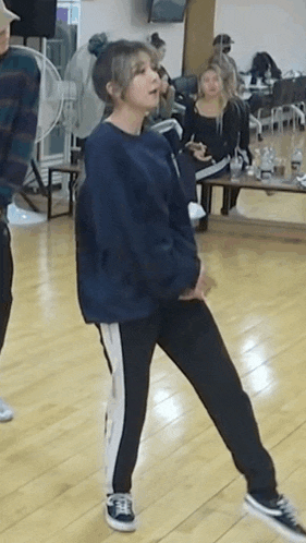 a woman in a blue sweater and black pants is dancing on a wooden floor in a room .