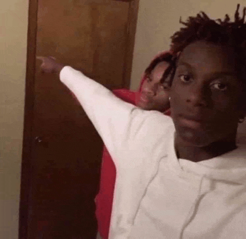 two young men are standing next to each other in front of a door . one of the men is pointing at the camera .