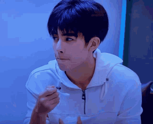a young man in a white hoodie is eating something with a fork