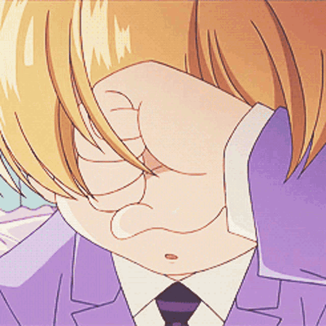 a man in a purple suit and tie covering his face with his hand