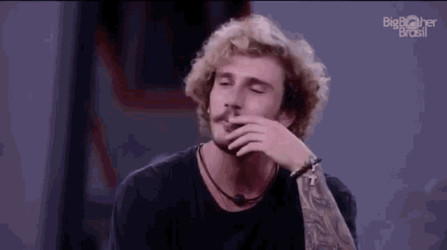 a man with blonde curly hair and a mustache is covering his mouth with his hand .