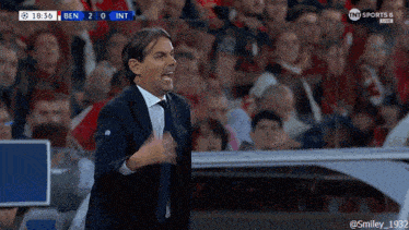 a man in a suit and tie stands in front of a crowd during a soccer match
