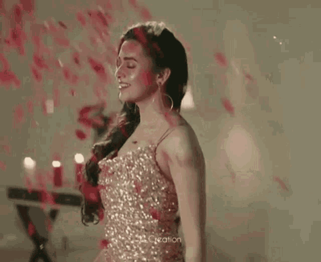 a woman in a pink sequined dress is standing in a room with roses on the floor .