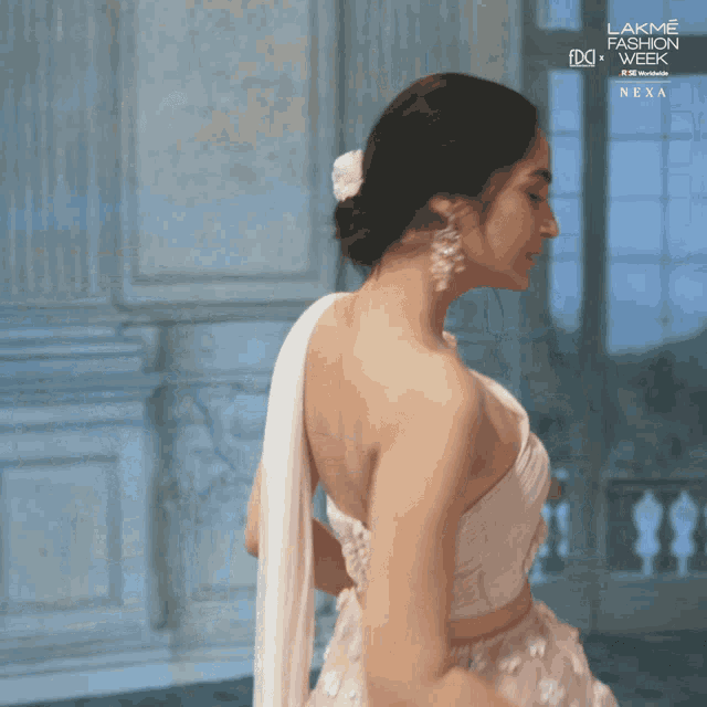 a woman in a white dress is standing in front of a window that says lakme fashion week next to her