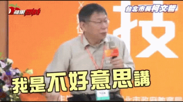 a man speaking into a microphone in front of an orange background with chinese writing on it