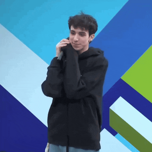 a young man wearing a black hoodie is holding a microphone