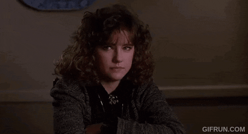 the woman is sitting at a table with her arms crossed and looking at the camera .