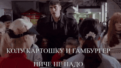 a man in a black jacket stands in front of a crowd of people and says " koly kartosku i hamburger " in russian