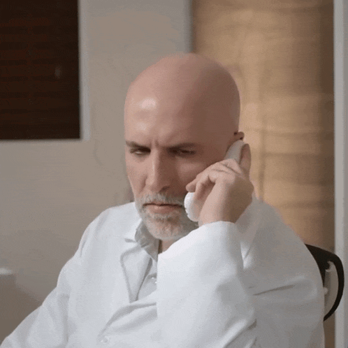 a bald man with a beard is talking on a cellphone