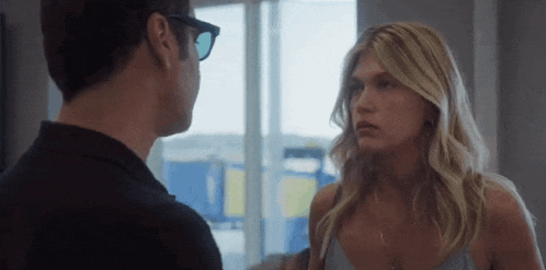 a man and a woman are standing next to each other and looking at each other . the woman is wearing sunglasses .