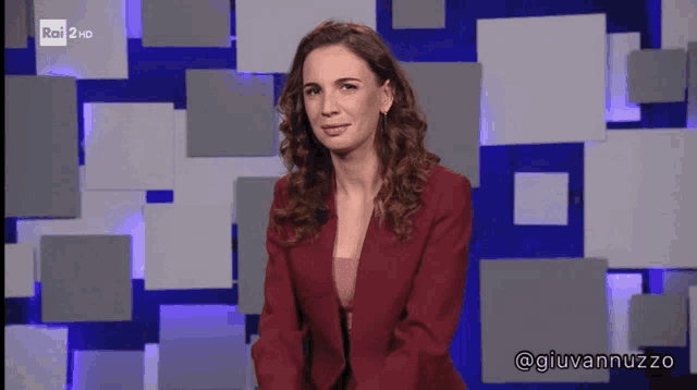 a woman in a red jacket is standing in front of a rai 2 hd screen