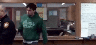 a man in a green hoodie is standing in front of a police officer .