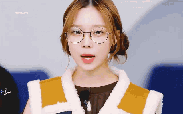 a woman wearing glasses and a fur vest is looking at the camera