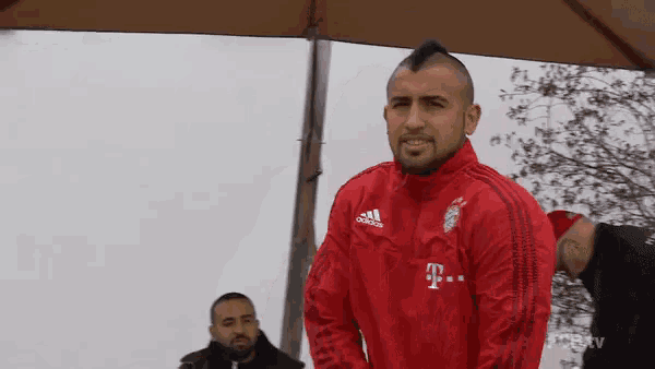 a man wearing a red adidas jacket with a t on it