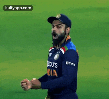 a man with a beard wearing a blue jersey and a baseball cap is walking on a field .