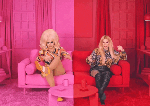two drag queens sitting on a pink and red couch