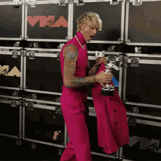 a man in a pink suit is holding a trophy in front of a wall that says vma