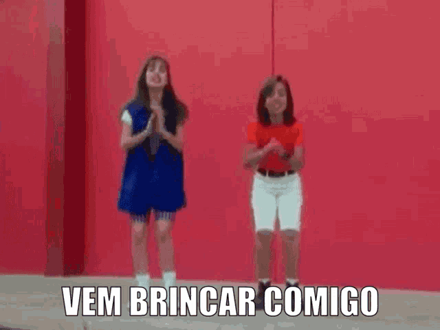 two little girls are jumping in front of a red wall with the words vem brincar comigo written below them