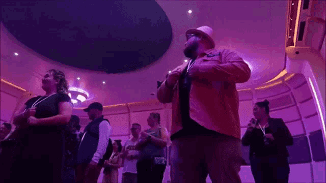 a group of people are standing in a room with purple lights and a man wearing a jacket that says ' captain '