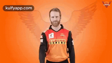 a man in a red and black cricket jersey is standing in front of a wall with the word four on it .