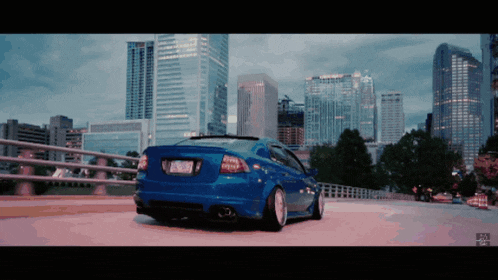 a blue car is parked on a bridge in front of a skyline