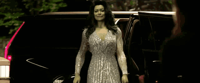 a woman in a silver dress is standing in front of a black suv .