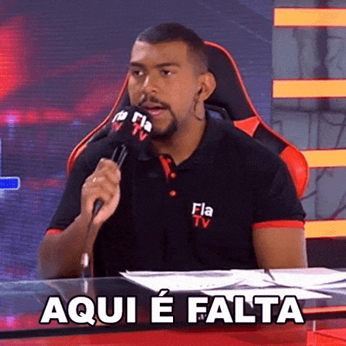 a man sitting at a desk with a microphone and the words aqui e falta written on the table