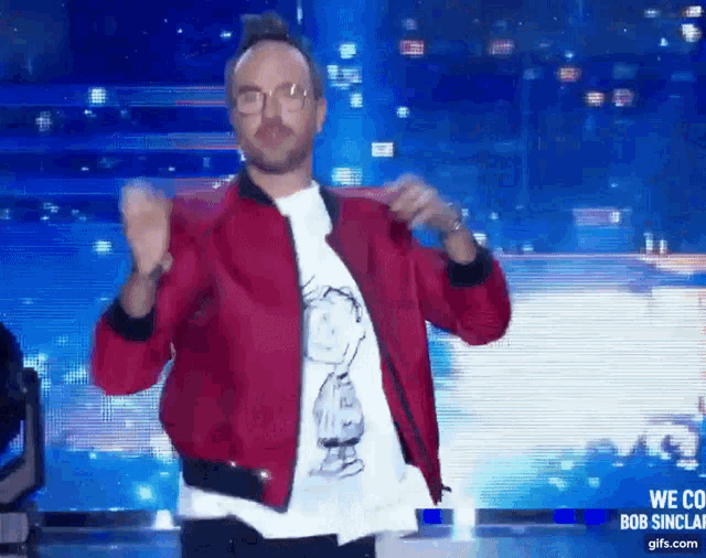 a man in a red jacket and a snoopy shirt is dancing on stage