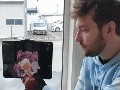 a man in a blue hoodie is holding a tablet with a picture of a doll on it