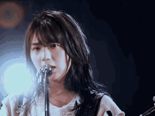 a woman singing into a microphone with a guitar in the background