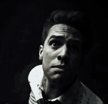a man in a white shirt and tie is making a funny face in a dark room .