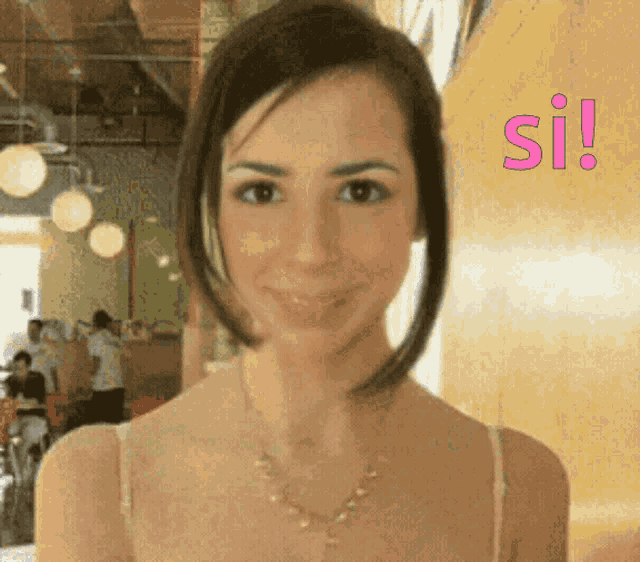 a woman in a white tank top is smiling in front of a sign that says si