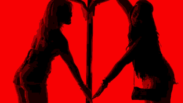 two women are making a heart shape with their hands against a red background