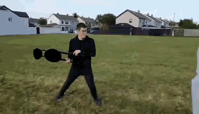 a man in a black shirt is standing in a grassy field holding a hammer .